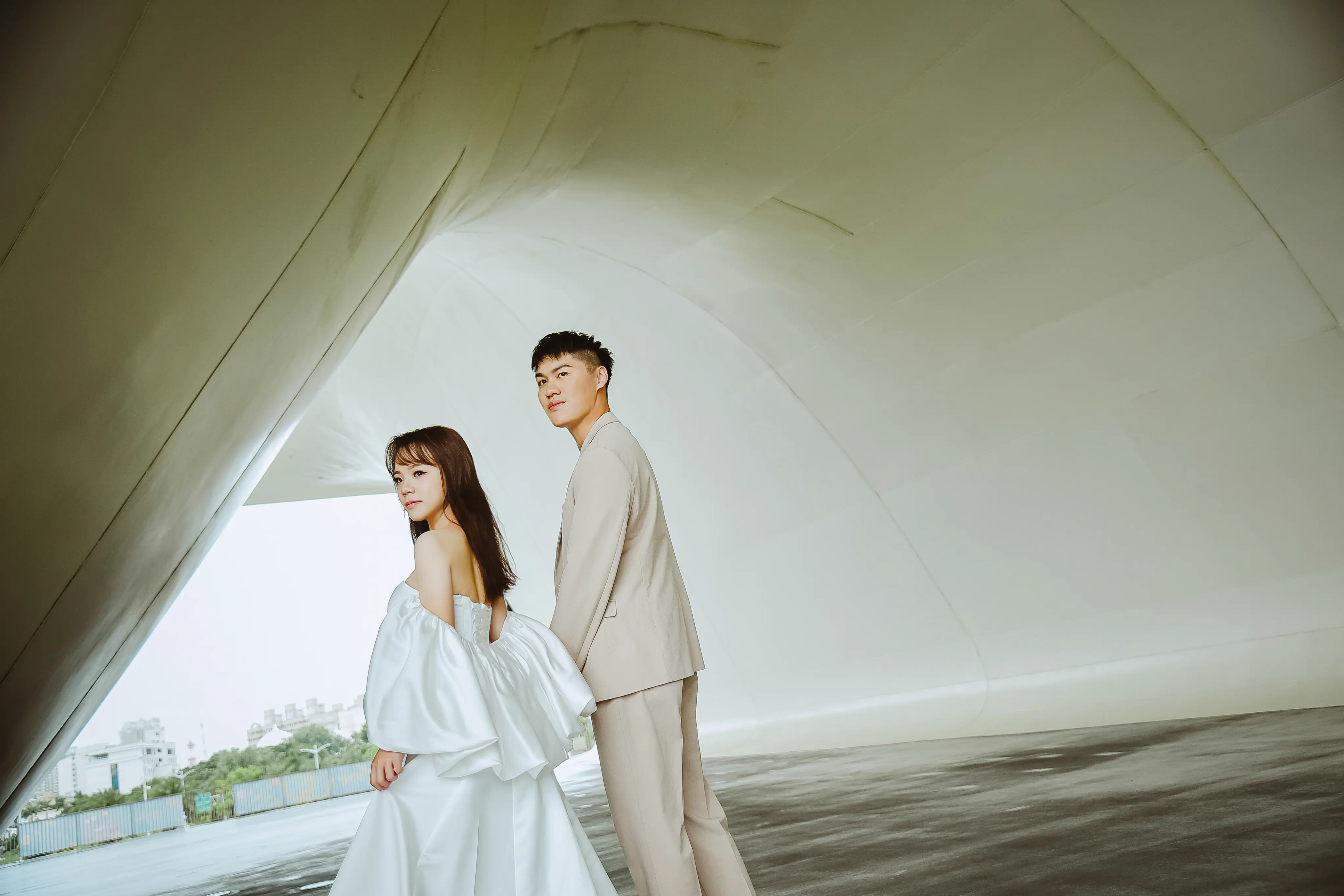 高雄現代婚紗攝影：新人穿白紗與淺色西裝站在建築前