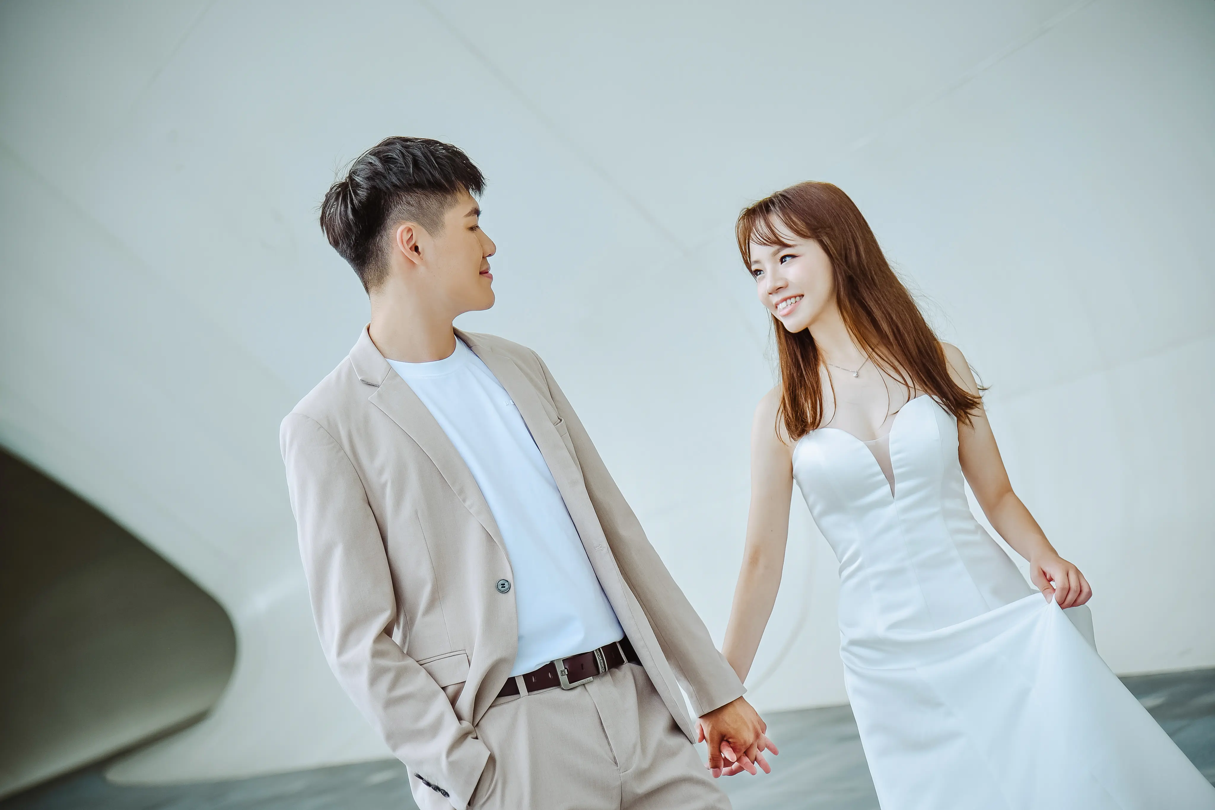 高雄婚紗攝影：新人穿淺色西裝與白紗在建築前牽手