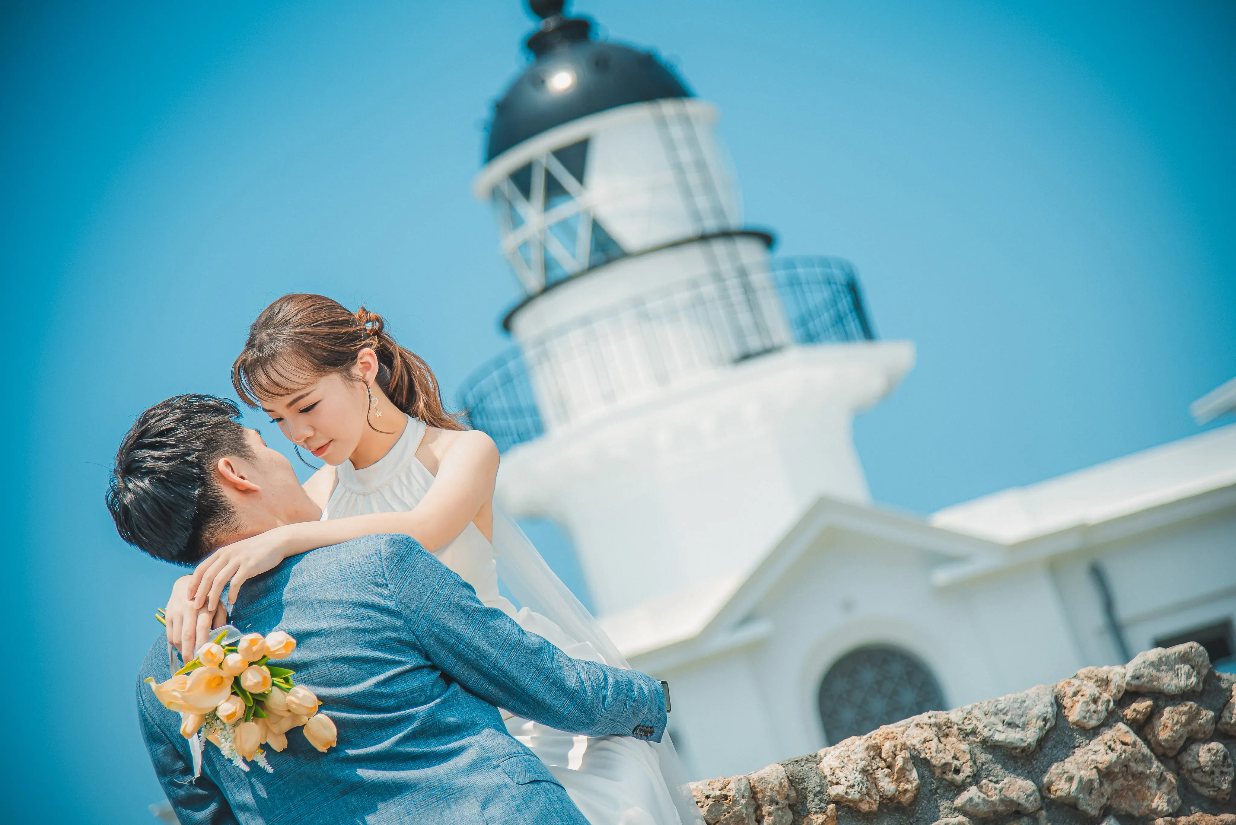 高雄婚紗攝影：藍色西裝新郎抱起白紗新娘，在燈塔前親吻