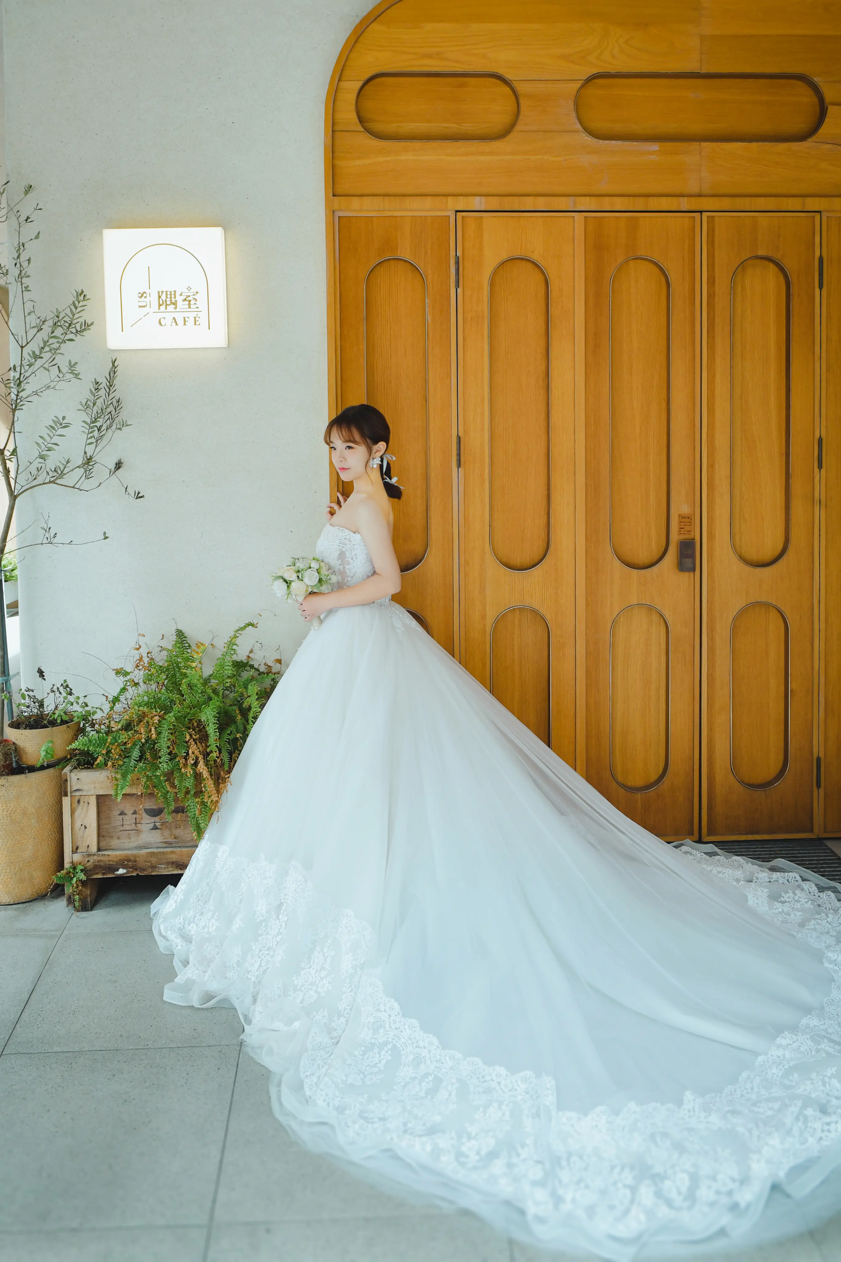 典雅白紗寫真：新娘穿蓬裙婚紗，站在木質大門與花藝旁