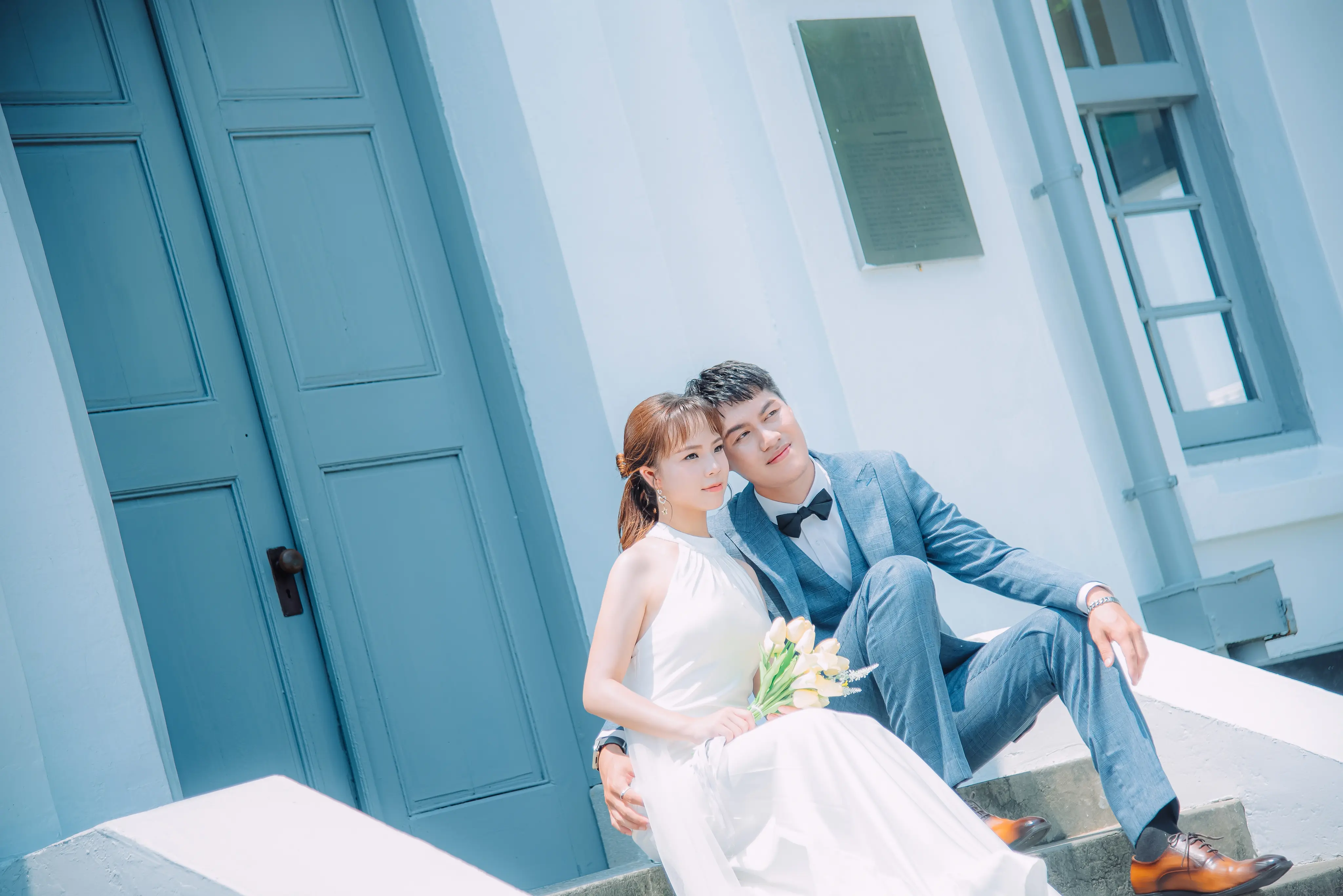 清新婚紗照：新人坐在藍色建築旁，自然靠近親密互動