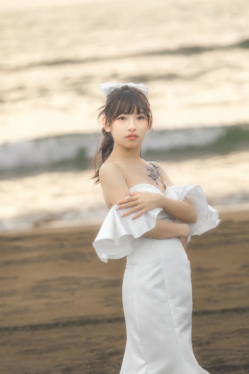 女生穿露肩緞面魚尾禮服，在海邊交疊雙臂望向鏡頭