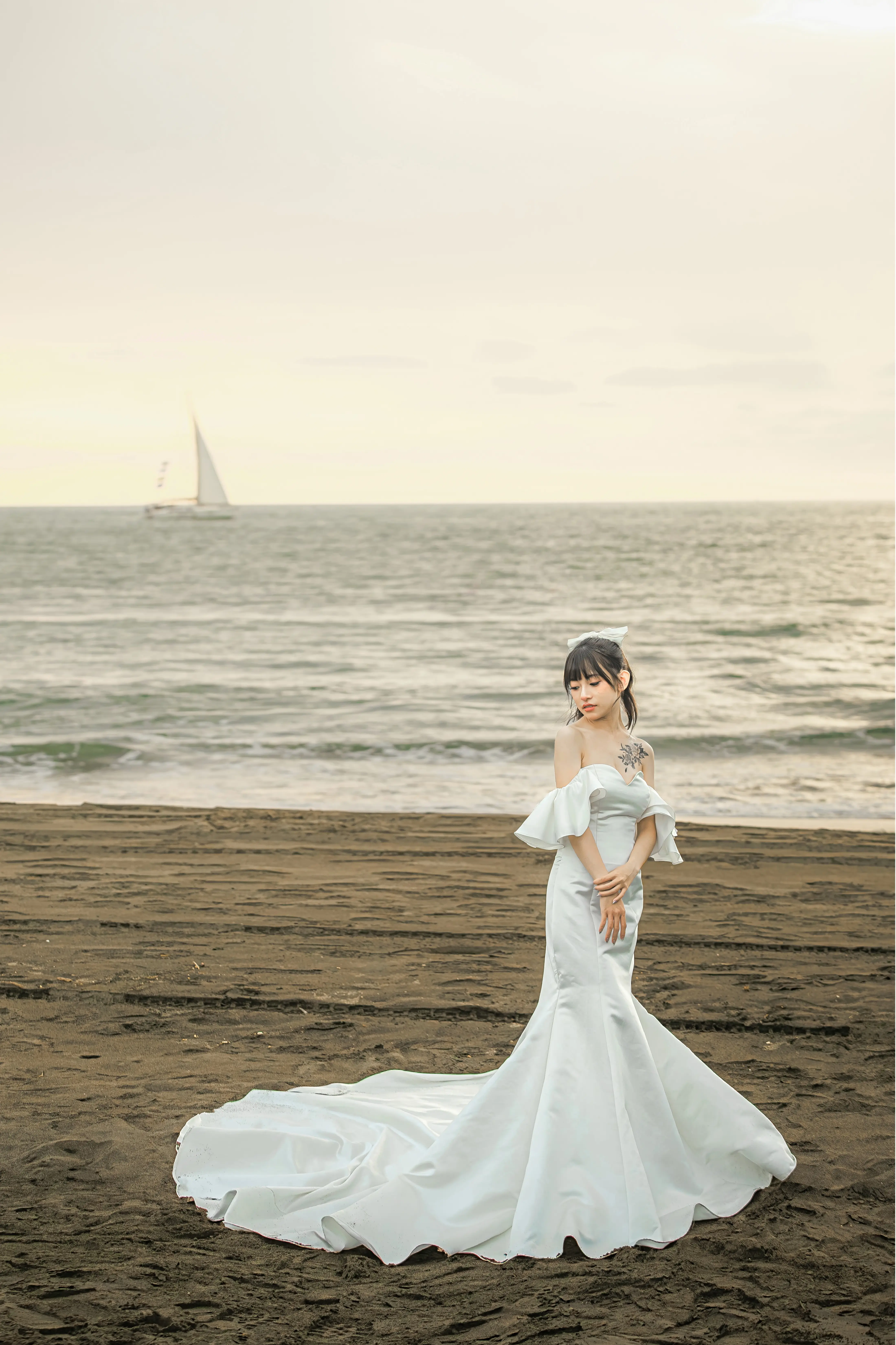 女生穿緞面魚尾禮服站在沙灘上，裙襬鋪展於身後