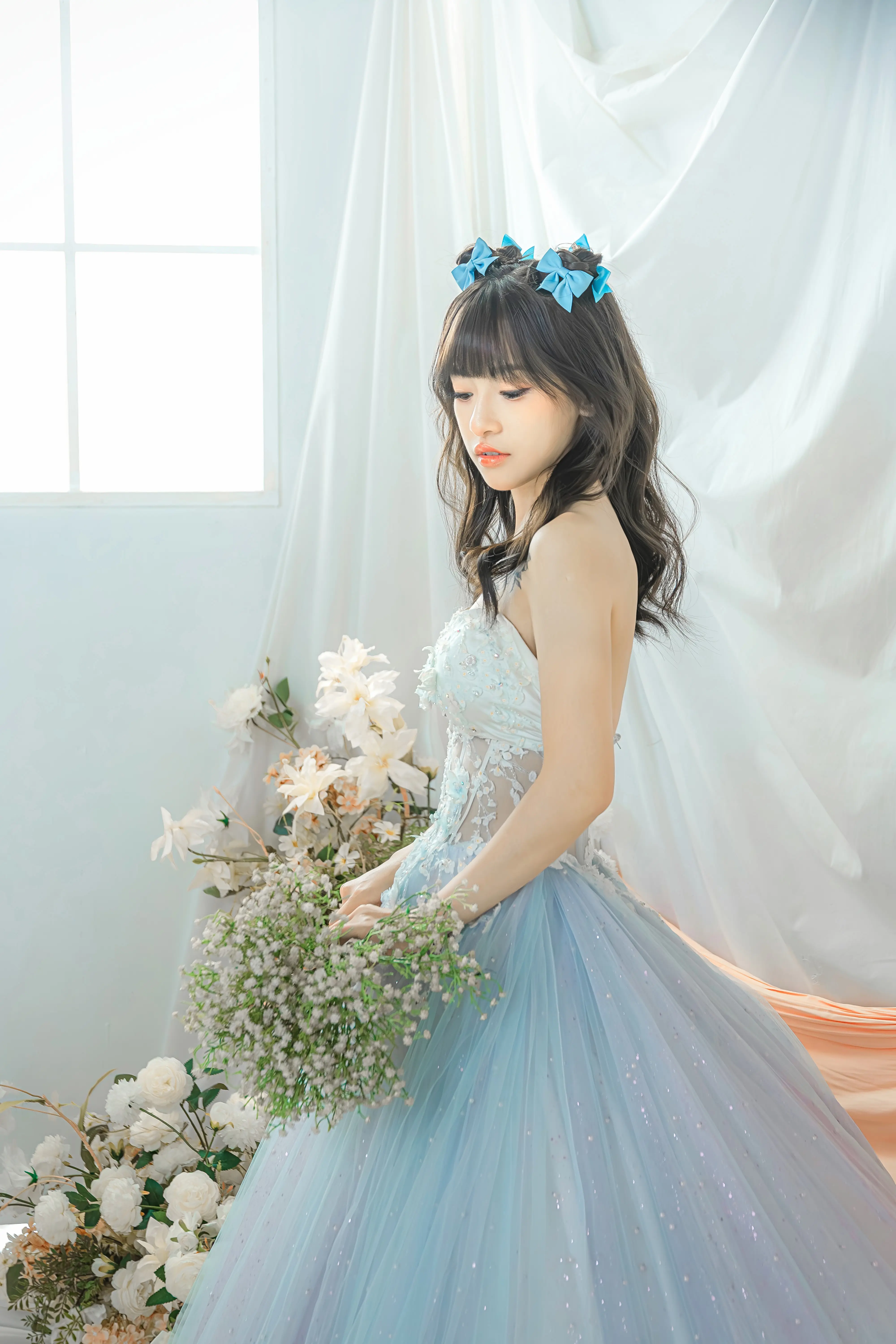 女生穿藍色蓬裙禮服手持捧花，站在淺色布幔前