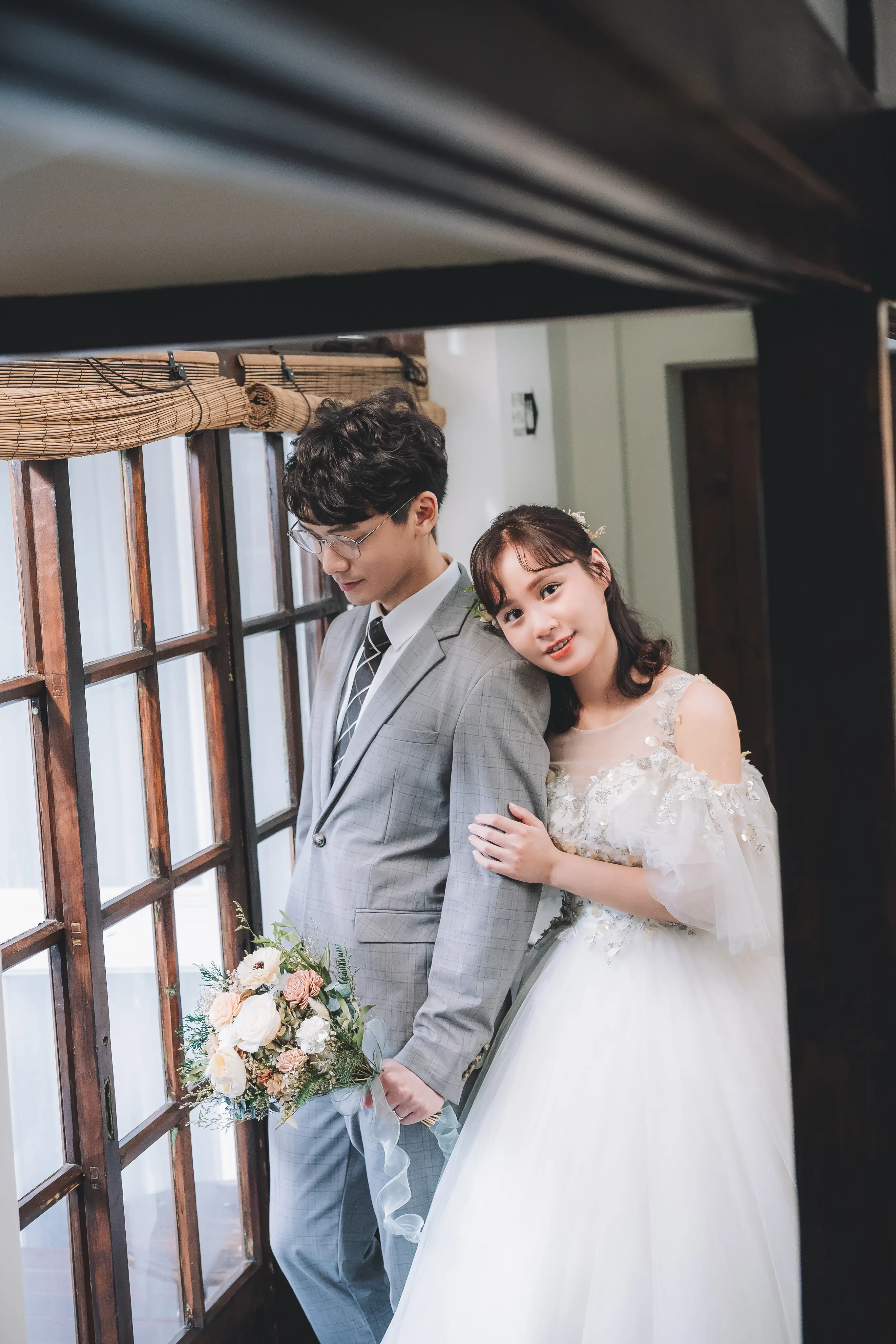 新娘在餐廳窗邊將頭靠在新郎肩上，兩人相依站立