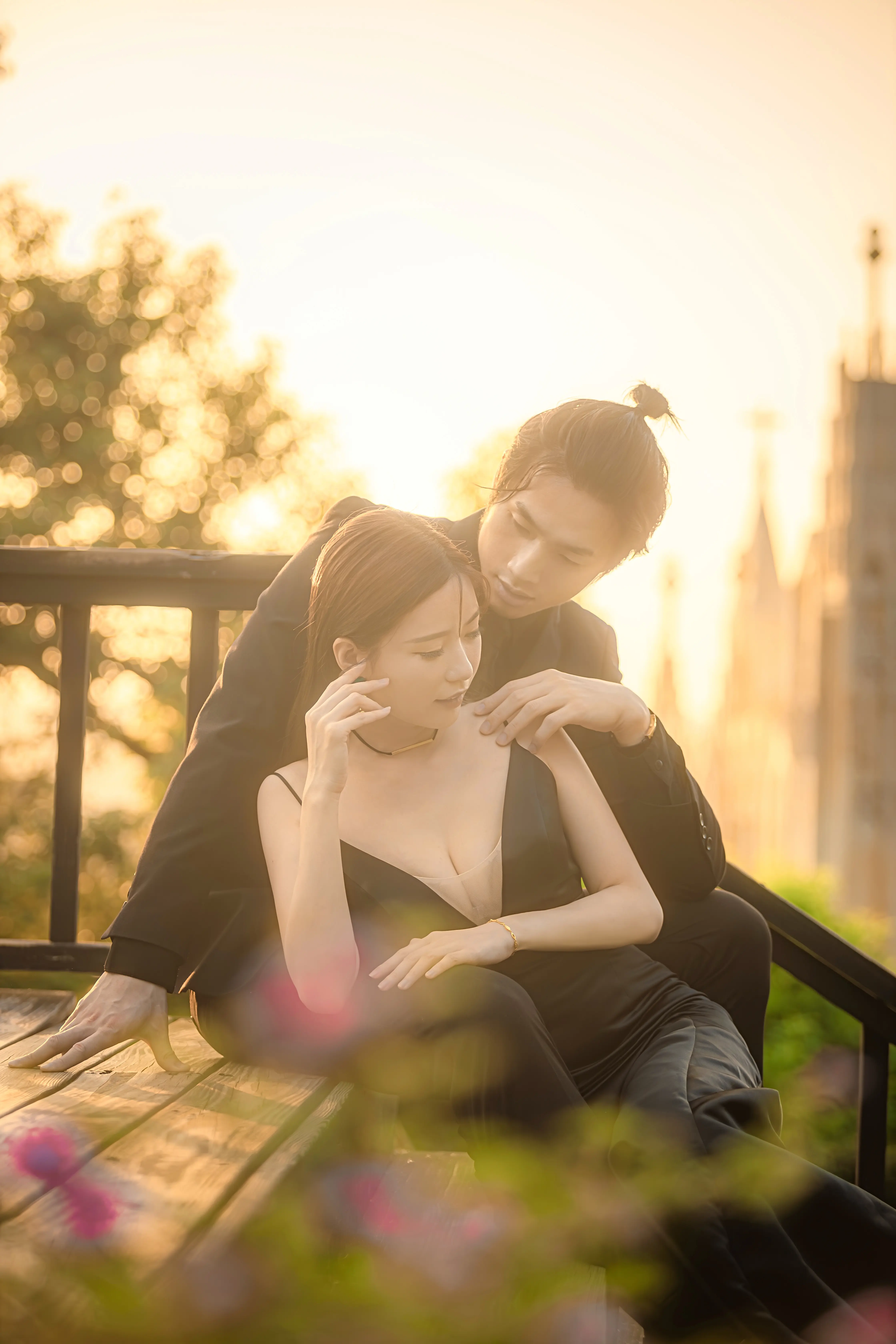 穿著黑色婚紗的新娘坐在戶外座椅上，新郎俯身靠近，背景映照暖色夕陽。