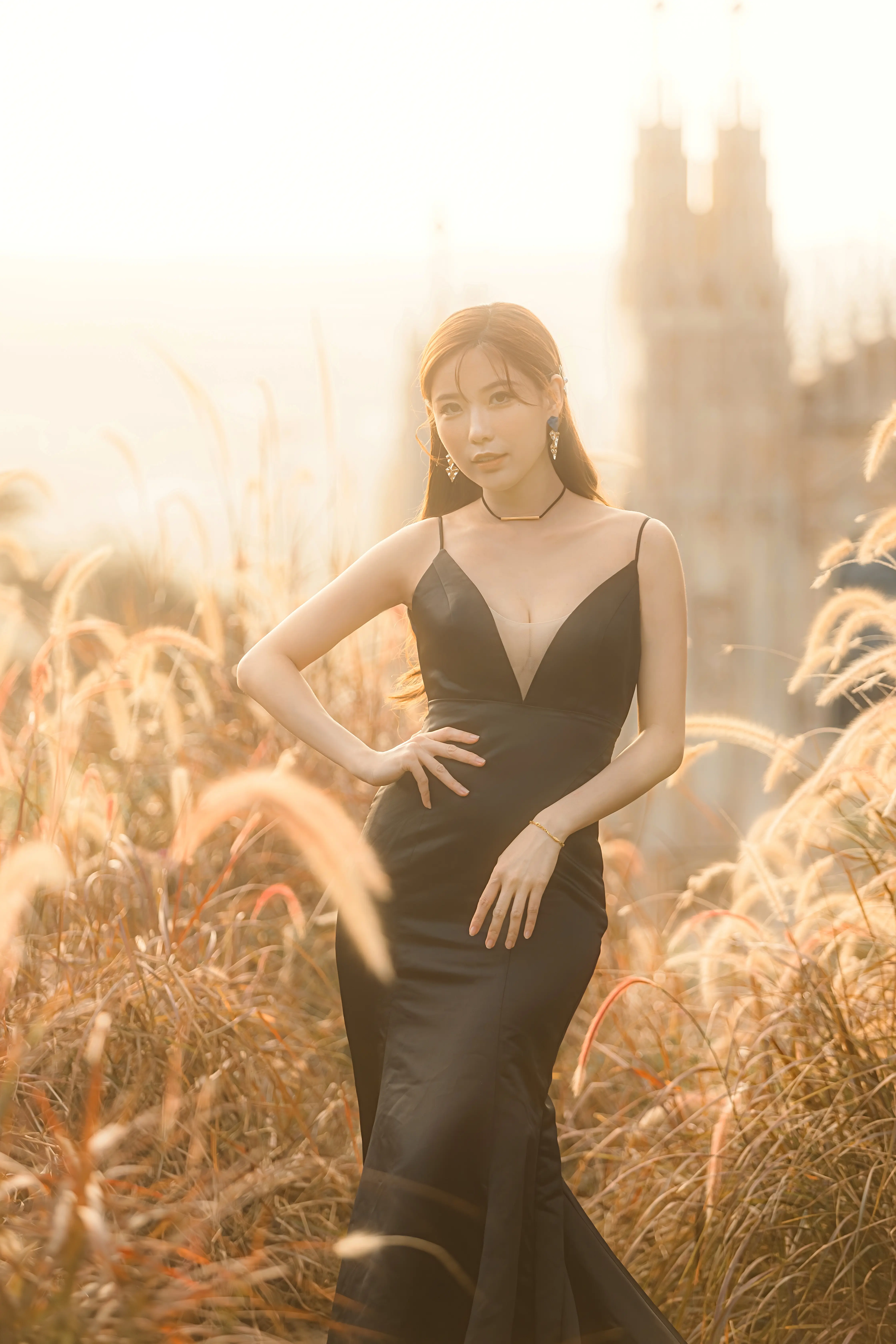 新娘穿著黑色婚紗站在夕陽映照的芒草間，展現修身禮服線條。