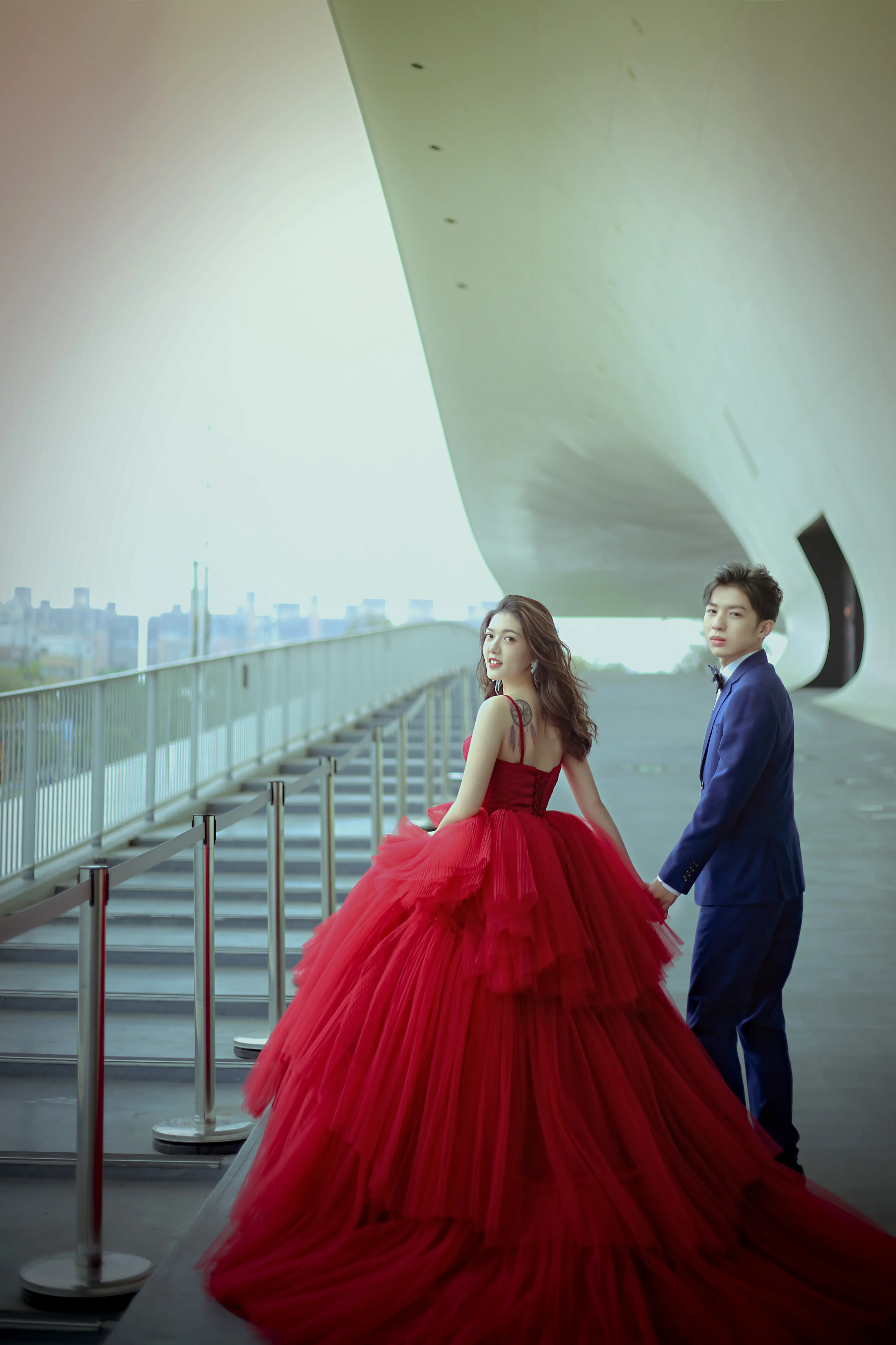 穿紅色蓬裙禮服的新人站在現代建築曲線牆面旁